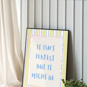 May include: Framed art print with the text "IT ISN'T PERFECT BUT IT MIGHT BE" in blue. The background has yellow and blue vertical stripes. The text is inside a pink, wavy border.