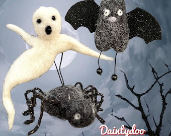 May include: Three felt Halloween ornaments: a white ghost, a black bat with glitter, and a black spider. The ornaments are hanging from a string.