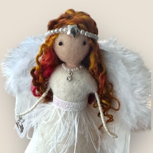 May include: A handmade angel doll with a white dress, feathered wings, and red and yellow curly hair. The doll has a pearl and silver headpiece, a pearl necklace with a crystal pendant, and a silver charm. The angel's dress has a sparkly belt.