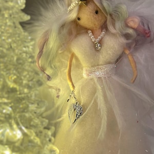 May include: A handmade angel figurine with a white dress and feathered wings. The angel has long, flowing hair with pastel highlights and wears a pearl necklace and a star-shaped crown. It holds a charm with silver wings.