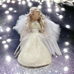 May include: A handmade angel doll with a cream-colored dress, feathered wings, and a star-adorned halo. The doll has long, wavy blonde hair and is holding a silver accessory. The dress is embellished with iridescent sequins and delicate lace trim.