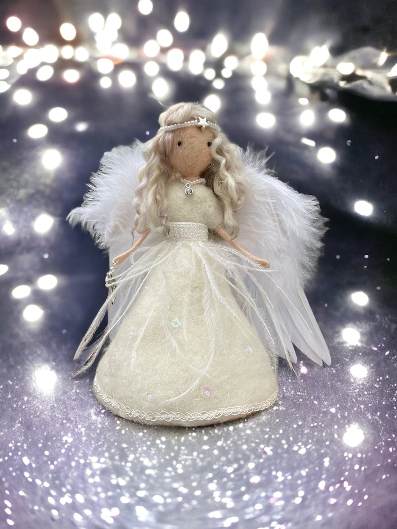 May include: A handmade angel doll with a cream-colored dress, feathered wings, and a star-adorned halo. The doll has long, wavy blonde hair and is holding a silver accessory. The dress is embellished with iridescent sequins and delicate lace trim.