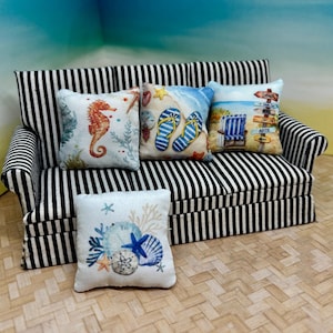 May include: Miniature black and white striped sofa with four decorative pillows. The pillows feature beach-themed designs, including a seahorse, flip-flops, beach chairs, and seashells. The pillows are square and have a white background.
