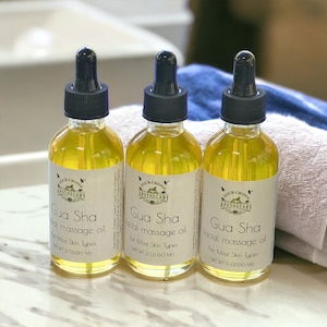 May include: Three glass bottles of Gua Sha facial massage oil with black droppers. Each bottle has a white label with the text "Four Crows Apothecary" and "Gua Sha facial massage oil". The bottles are filled with a yellow liquid and are 2 oz (60 ml).