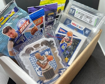 May include: A cardboard box filled with basketball trading cards and unopened packs. The box contains a graded Anthony Edwards rookie card, NBA Hoops cards, and a Kevin Garnett Crown Royale card. Text on the box reads "Example of possible contents."