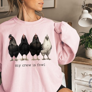 Puede incluir: Una sudadera rosa con un gráfico de cinco pollos y el texto "my crew is fowl".