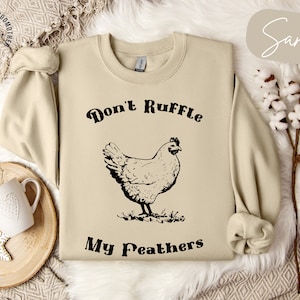May include: A beige sweatshirt with the text "Don't Ruffle My Feathers" and a black and white illustration of a chicken.
