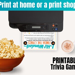 May include: A black printer feeding a white sheet of paper with a 1-Hit Wonders Finish the Lyrics trivia game printed on it, positioned next to a brown bowl filled with popcorn and a white mug containing a light brown beverage.