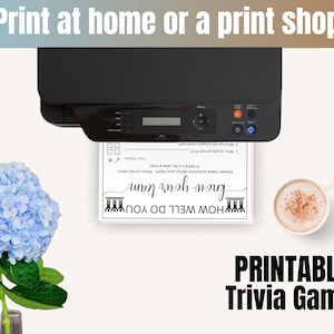 May include: A black printer outputting a white sheet of paper with the text "HOW WELL DO YOU know your team" and trivia questions. To the left is a blue hydrangea flower, and to the right is a white mug filled with a light brown beverage.
