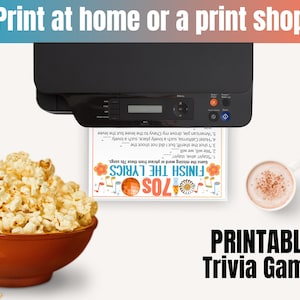 May include: A black printer printing a trivia game sheet with the text "Finish the Lyrics 70s". A bowl of popcorn and a cup of coffee are on the table. The text "Print at home or a print shop" is at the top.