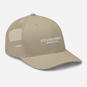Op de afbeelding: Een beige truckercap met een wit geborduurd logo met de tekst "KOUNKHMER ANGKRN DNA".