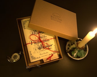 May include: A brown box with a red ribbon tied around it. The box contains a game called "Murder in the Victorian Manor" with a booklet and pencils. The box is open and the game is visible. There is a pocket watch and a candle in the background.