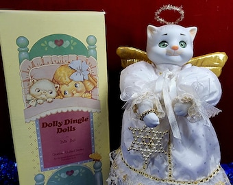May include: A white porcelain cat angel figurine with gold wings and a halo. The angel is wearing a white dress with gold trim and holding a snowflake ornament. The figurine is packaged in a box with a picture of a cat and a girl in a bed.