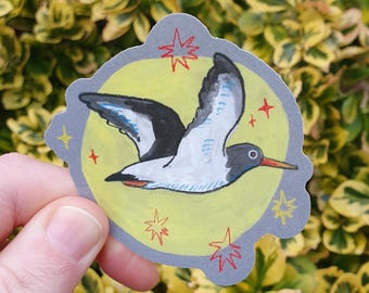 May include: A sticker featuring a stylized illustration of a bird in flight. The bird has black, white, and blue wings, a red beak, and a yellow body. The sticker is surrounded by a gray border with red star accents and a yellow background.