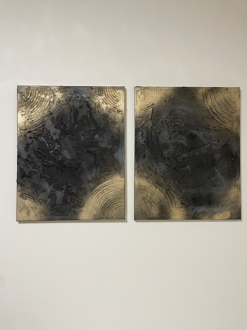 May include: Two square abstract paintings with a black and gold color scheme. The paintings have a textured surface and a circular pattern.