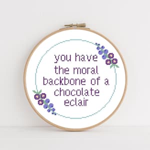 May include: A white embroidery hoop with a light blue background and purple flowers. The text reads "You have the moral backbone of a chocolate éclair."