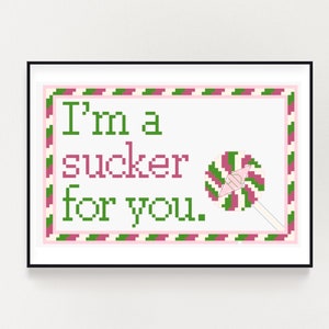 Pode incluir: Padrão de ponto cruz com uma borda rosa e verde e o texto "I'm a sucker for you." com uma pirulito rosa e verde no canto.