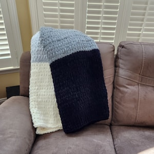May include: A soft, chunky knit throw blanket in shades of gray, white, and black. The blanket is draped over a brown leather couch.