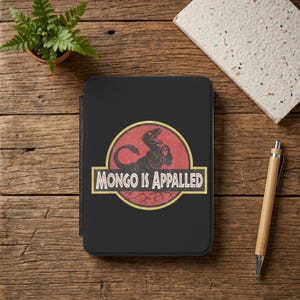 May include: A black tablet case featuring a circular graphic with a distressed red background and a black dinosaur silhouette. The text "MONGO IS APPALLED" is printed in white capital letters within a yellow-bordered rectangular banner.