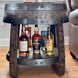 May include: A rustic wooden barrel table with a metal top and a lower shelf. The table is decorated with metal accents and has four legs. There are five bottles of liquor on the table, including Old Forester 1870, Weller 12 Year Old, and Jeppson's Mal&ouml;rt Liqueur.
