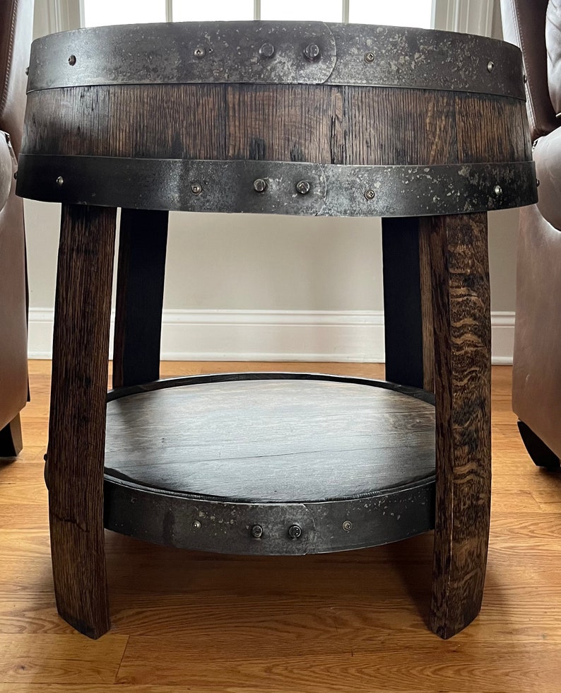 May include: A round wooden table with a metal band around the top and bottom. The table has a lower shelf and is made from reclaimed wood.