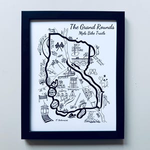 May include: Black framed print of a hand-drawn map of the Grand Rounds bike trails in Minneapolis. The map is in black and white, with detailed illustrations of landmarks and recreational areas. Text at the top reads "The Grand Rounds Mpls Bike Trails."