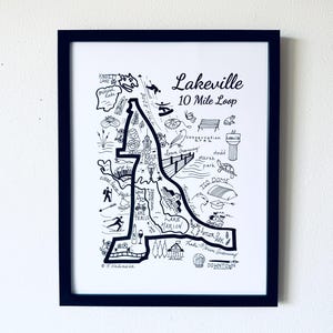 May include: Black framed art print featuring a hand-drawn map of Lakeville, with the text "Lakeville 10 Mile Loop". The map includes illustrations of local landmarks and activities, all in black and white.