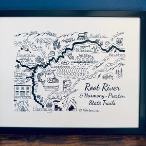 May include: A framed black and white line art map titled Root River & Harmony-Preston State Trails. The illustration features landmarks, towns like Lanesboro and Harmony, rivers, and icons including a fish, a canoe, and an owl, all set within a simple black frame.