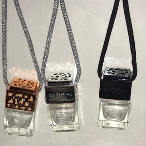 May include: Three car air fresheners with clear glass bottles and decorative metal tops. One is copper-colored, one is silver, and one is black. Each has a string for hanging and the text "Car Perfume".