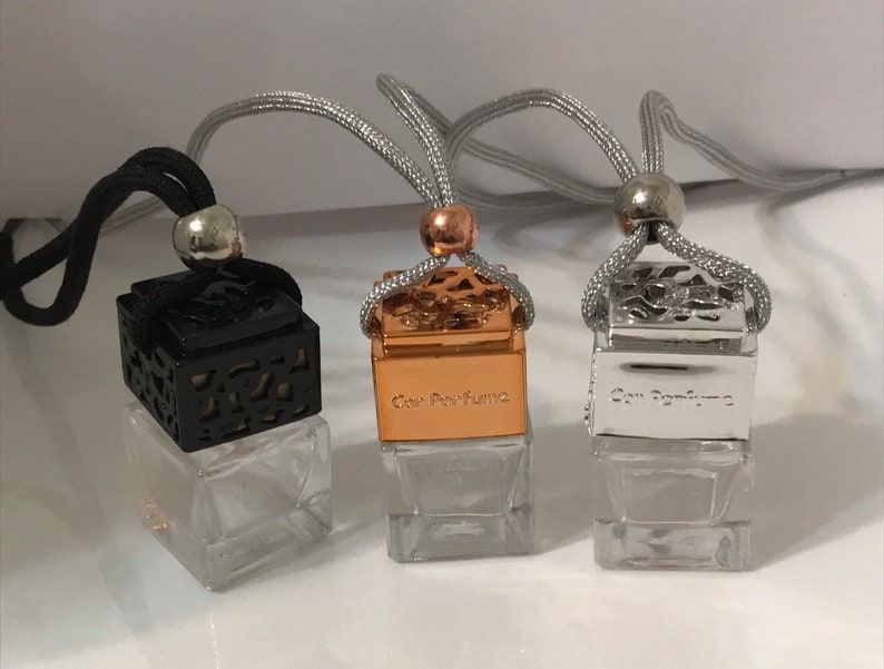 May include: Three car air fresheners with clear glass bottles and decorative tops. One has a black top, one a gold top, and one a silver top. Each has a silver or black cord for hanging. The text "Car Perfume" is visible on the gold and silver tops.