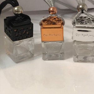 May include: Three car air fresheners with clear glass bottles and decorative tops. One has a black, openwork top, another a copper-colored top with "Car Perfume" printed on it, and the third a silver top. Each has a cord for hanging.