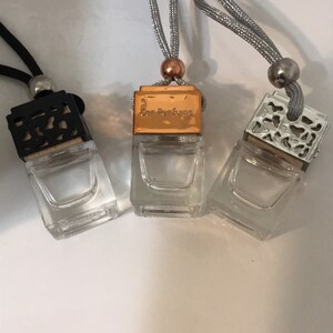 May include: Three small, clear glass car air fresheners with decorative tops and silver cords. One has a black top, one a gold top with "Car Perfume" text, and the third a silver top. The cords are silver and black.