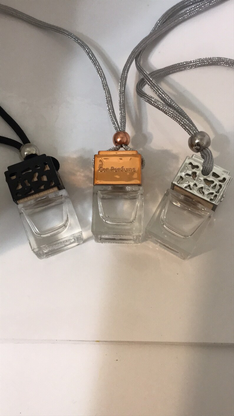 May include: Three small, clear glass car air fresheners with decorative tops and silver cords. One has a black top, one a gold top with "Car Perfume" text, and the third a silver top. The cords are silver and black.