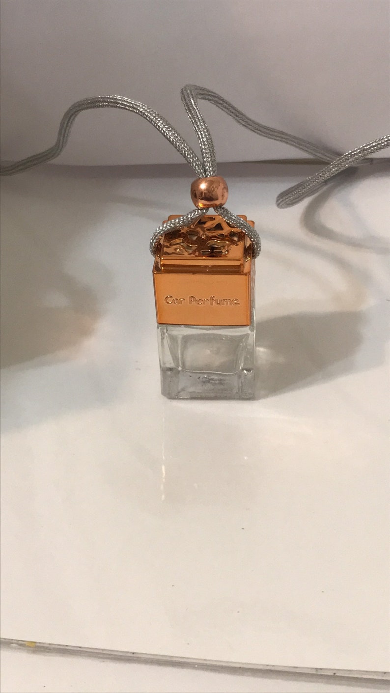 May include: A small, clear glass car perfume bottle with a copper-colored top and a silver cord for hanging. The top is engraved with the words "Car Perfume". The bottle is empty.