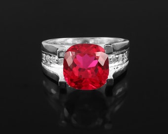 May include: A silver ring with a large, red, cushion-cut gemstone surrounded by smaller, clear gemstones.