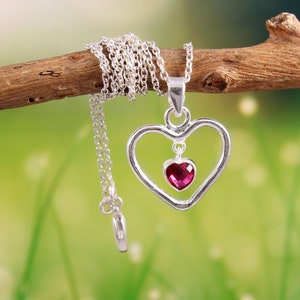 May include: A silver necklace with a double heart pendant. The pendant features a smaller heart with a pink gemstone in the center.