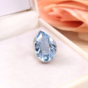 Puede incluir: Una piedra preciosa azul claro en forma de l&aacute;grima engastada en un anillo de plata.