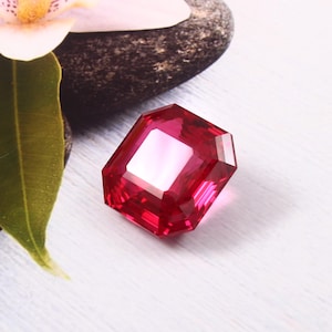 Może przedstawiać: Jaskrawoczerwony kamień szlachetny o kwadratowym szlifie szmaragdowym. Kamień szlachetny umieszczony jest na białym tle.