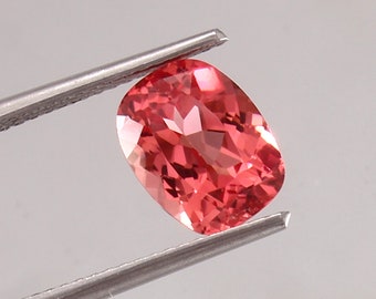 Pode incluir: Uma gema rosa vibrante, de forma oval e talhada com facetas. A gema é segurada por uma pinça.