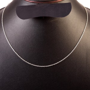 Puede incluir: Un collar de cadena de plata en un expositor negro.