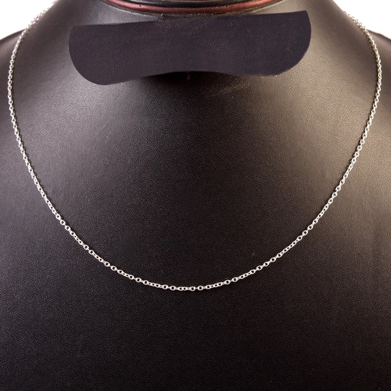 Puede incluir: Un collar de cadena de plata en un expositor negro.