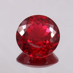 May include: A deep red gemstone with a round cut and a high polish. The gemstone is set against a white background.