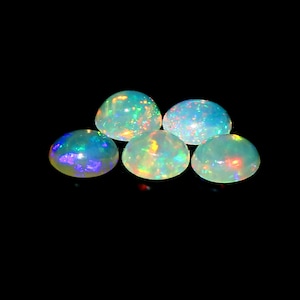 May include: Five iridescent opal cabochons with a polished, domed surface. The opals display a play of color with flashes of blue, green, yellow, and red against a milky white base. The gemstones are set against a black background.