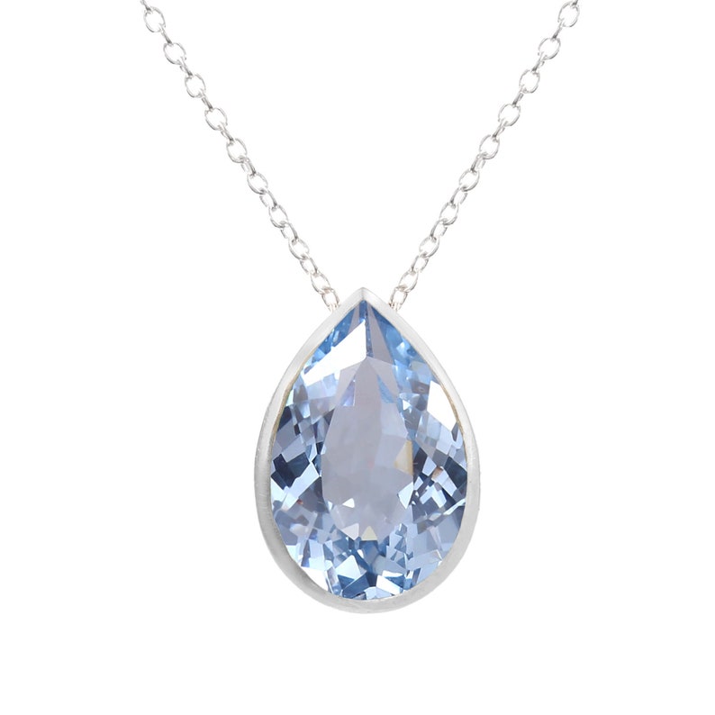 Puede incluir: Un collar de cadena de plata con un colgante en forma de l&aacute;grima con una piedra preciosa azul claro.