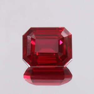 Puede incluir: Una piedra preciosa de color rojo intenso de talla esmeralda con un alto pulido.