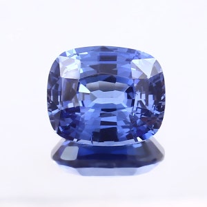 Op de afbeelding: Een kussen geslepen saffier edelsteen met een diepe blauwe kleur. De edelsteen is gefacetteerd en heeft een hoge mate van glans.