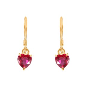 Può includere: Un paio di orecchini pendenti color oro. Ogni orecchino presenta una pietra preziosa rosso scuro a forma di cuore. Gli orecchini hanno un design semplice con chiusura a gancio e sono su sfondo bianco.