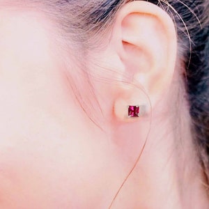 Puede incluir: Primer plano de una oreja con un pequeño pendiente cuadrado de piedra roja. El pendiente está engastado en un engaste de plata.