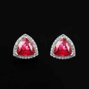 May include: A pair of silver earrings with a triangular red gemstone surrounded by a halo of smaller white gemstones.
