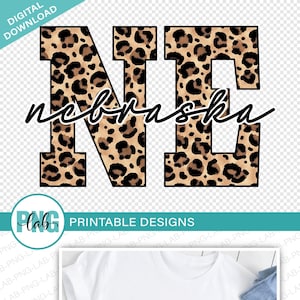 May include: A digital download of a graphic design featuring the letters "NE" in a leopard print pattern. The letters are outlined in black and the word "Nebraska" is written in cursive underneath. The design is shown on a white t-shirt.